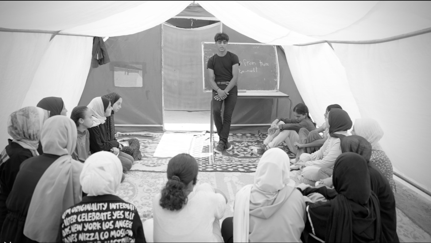 A young man teaching in a tent classroom